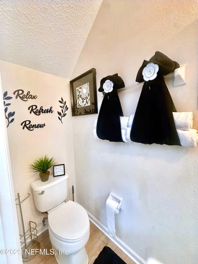 bathroom with baseboards, toilet, wood finished floors, vaulted ceiling, and a textured ceiling