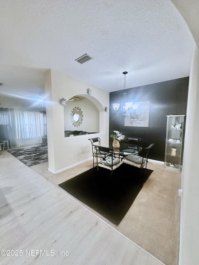 dining room featuring a notable chandelier, visible vents, light wood-style flooring, a textured ceiling, and baseboards