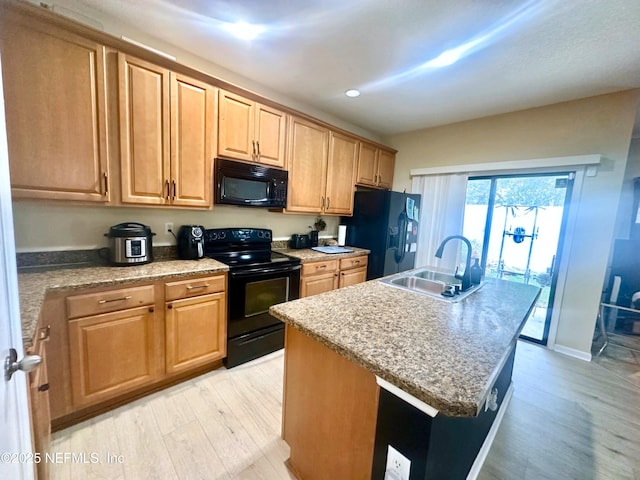 kitchen with light wood-style flooring, brown cabinetry, a sink, an island with sink, and black appliances