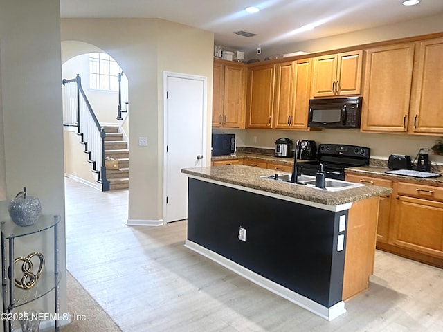 kitchen with a sink, light wood-style floors, black appliances, brown cabinetry, and a center island with sink