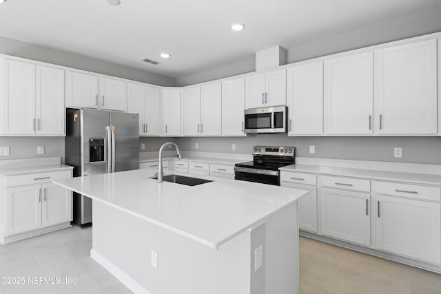 kitchen featuring a center island with sink, stainless steel appliances, light countertops, white cabinetry, and a sink