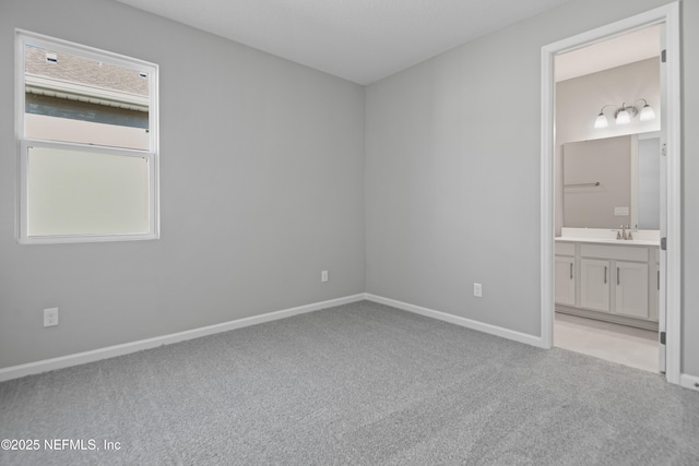 unfurnished bedroom with ensuite bath, baseboards, and light colored carpet