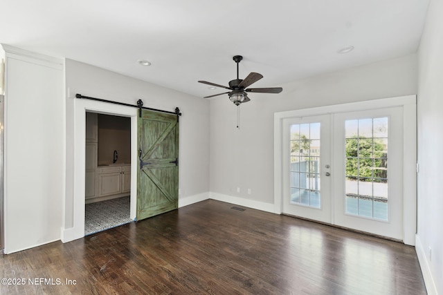 spare room featuring a barn door, visible vents, baseboards, dark wood-style floors, and french doors