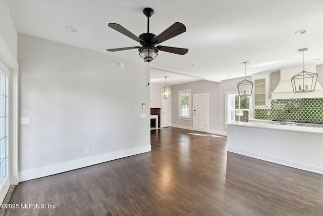 unfurnished living room featuring ceiling fan, a fireplace, baseboards, and dark wood-style flooring