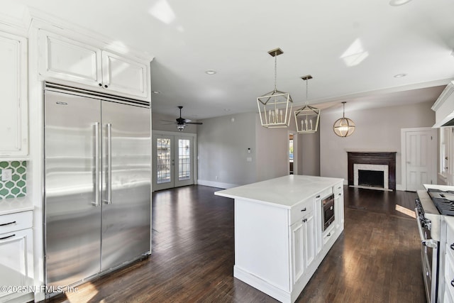 kitchen featuring built in appliances, a fireplace, white cabinetry, open floor plan, and light countertops