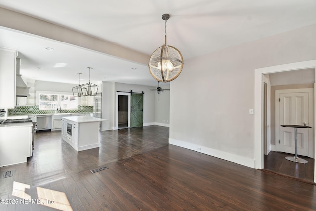 kitchen with a barn door, white cabinetry, open floor plan, light countertops, and dark wood finished floors