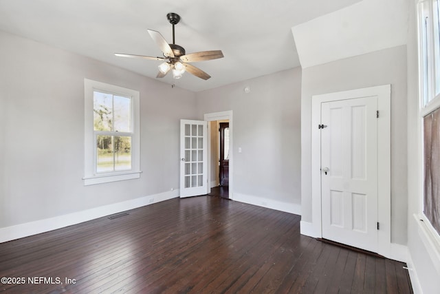 empty room with dark wood-type flooring, a ceiling fan, visible vents, and baseboards