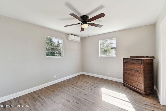 unfurnished bedroom featuring a wall unit AC, ceiling fan, baseboards, and wood finished floors