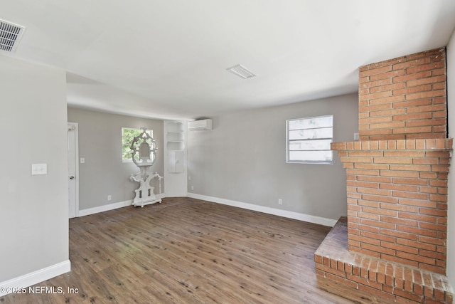 unfurnished living room featuring a wall unit AC, visible vents, baseboards, and wood finished floors