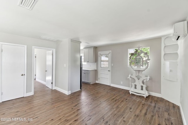 unfurnished living room with visible vents, a wall unit AC, baseboards, and wood finished floors