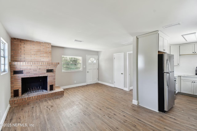 unfurnished living room featuring a brick fireplace, visible vents, light wood finished floors, and a healthy amount of sunlight