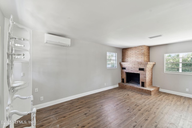 unfurnished living room featuring wood finished floors, visible vents, baseboards, a brick fireplace, and a wall mounted air conditioner