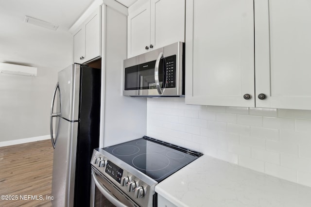 kitchen with stainless steel appliances, white cabinets, a wall mounted AC, light stone countertops, and tasteful backsplash