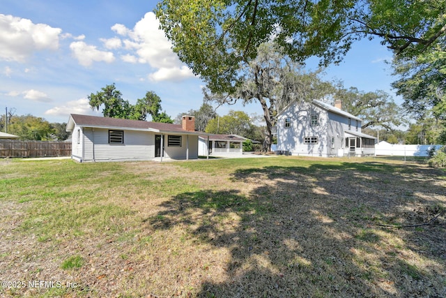 back of property with a chimney, fence, and a lawn