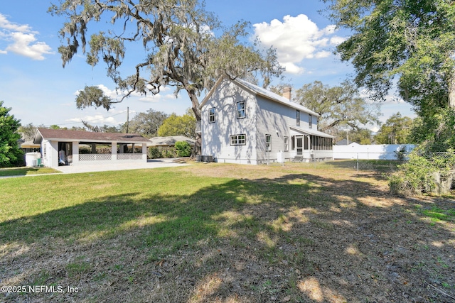 rear view of house featuring a yard, a chimney, a sunroom, fence, and an attached carport