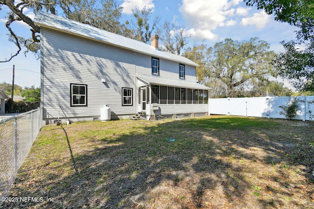 rear view of property featuring a sunroom, a fenced backyard, a chimney, a gate, and a yard