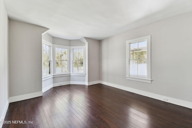 spare room featuring hardwood / wood-style flooring, visible vents, and baseboards