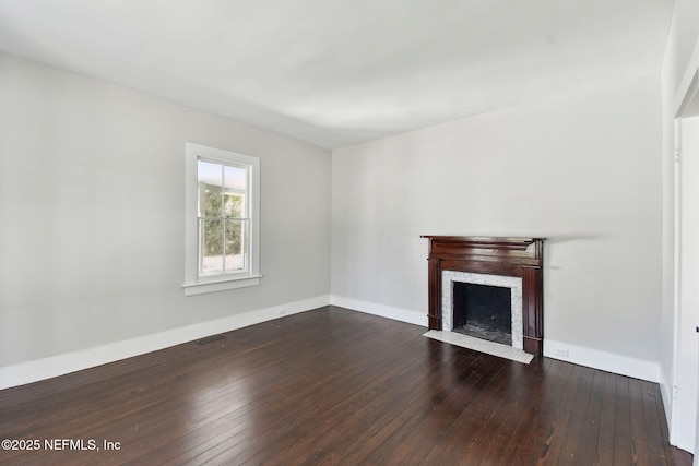 unfurnished living room featuring dark wood-style floors, baseboards, visible vents, and a fireplace with flush hearth