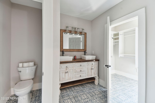 bathroom featuring baseboards, a sink, toilet, and double vanity