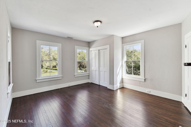 unfurnished bedroom featuring dark wood-style floors, a closet, visible vents, and baseboards