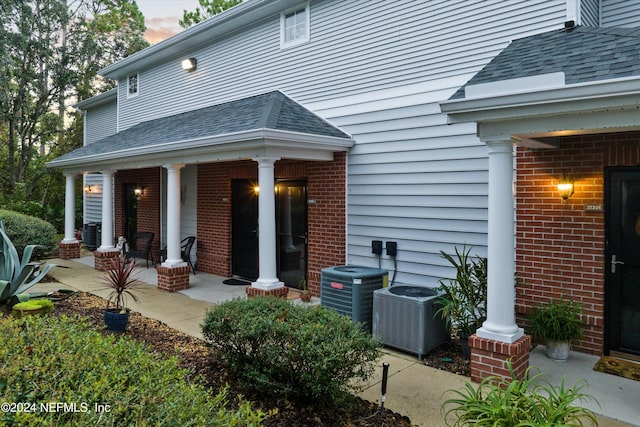 doorway to property featuring a shingled roof, cooling unit, and brick siding