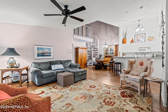 living area featuring ceiling fan with notable chandelier, wood finished floors, a towering ceiling, and stairs