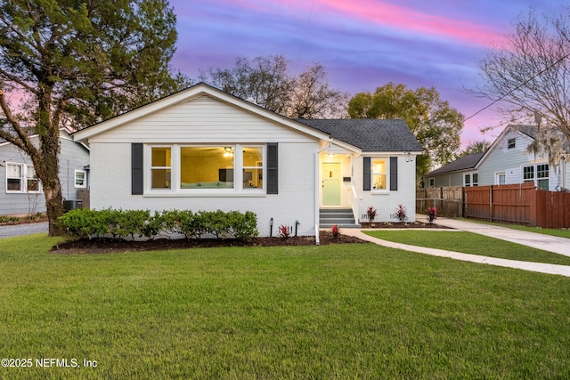 view of front of home featuring entry steps, fence, a lawn, and brick siding