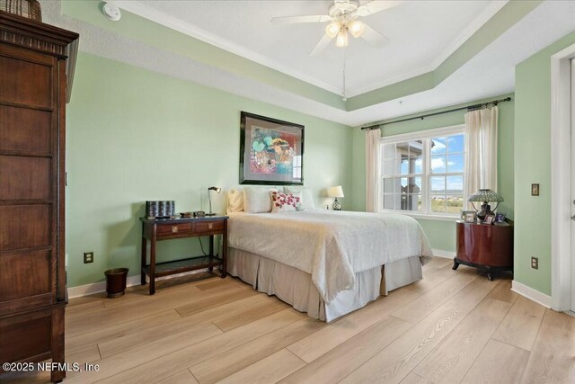 bedroom featuring baseboards, a raised ceiling, light wood-style floors, and crown molding