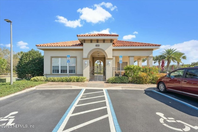 exterior space featuring a tile roof, stucco siding, uncovered parking, and a gate