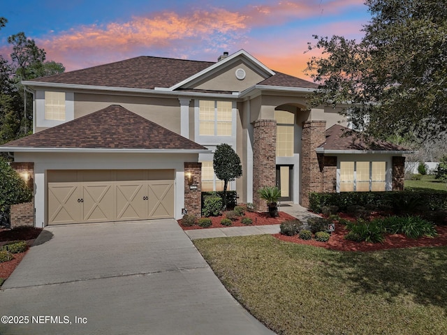 traditional home with stucco siding, a shingled roof, a front yard, a garage, and driveway