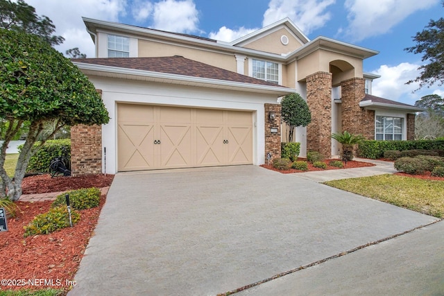 traditional home featuring a garage, driveway, brick siding, and stucco siding