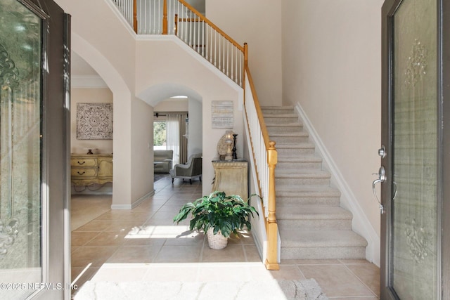 tiled foyer featuring a high ceiling, baseboards, stairs, and arched walkways