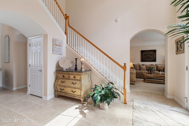 entryway featuring arched walkways, light tile patterned flooring, stairway, and a high ceiling