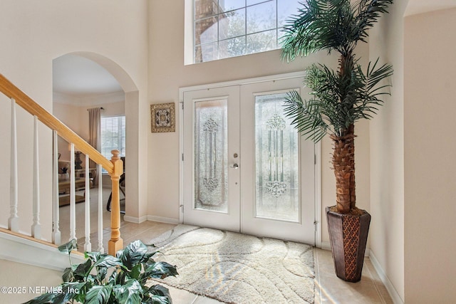 tiled entryway with baseboards, stairs, arched walkways, and french doors