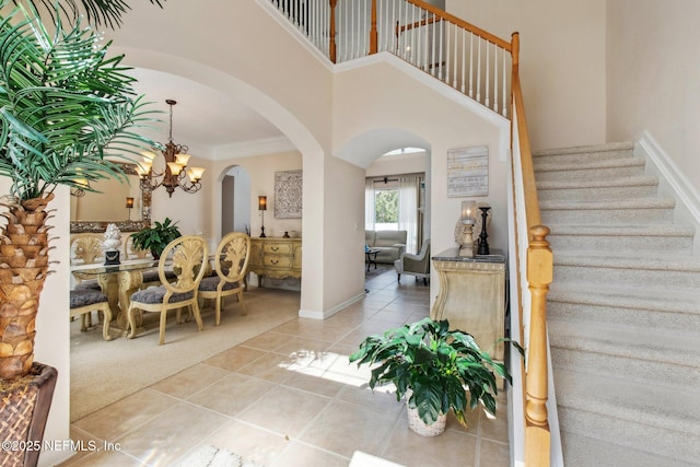 carpeted entrance foyer with arched walkways, crown molding, a high ceiling, tile patterned flooring, and stairs