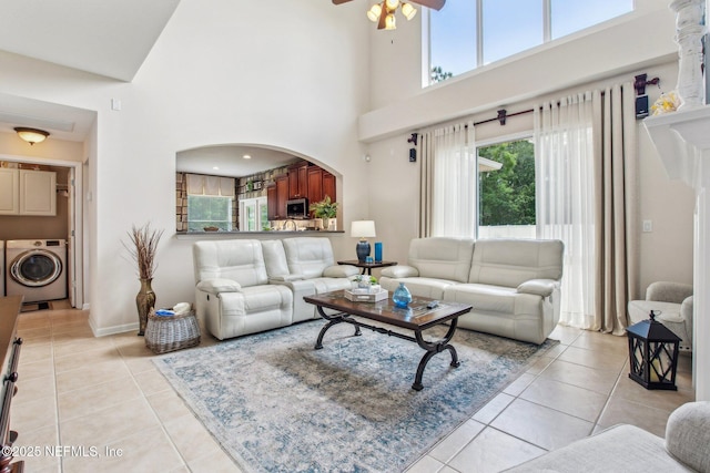 living area with ceiling fan, arched walkways, light tile patterned flooring, baseboards, and washer / dryer