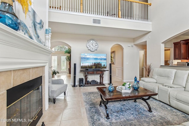 living room with arched walkways, light tile patterned floors, a tile fireplace, a high ceiling, and visible vents