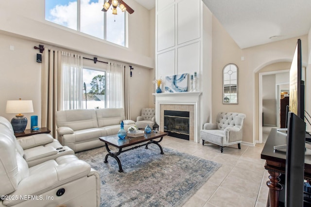 living room with a fireplace, light tile patterned floors, a towering ceiling, ceiling fan, and baseboards