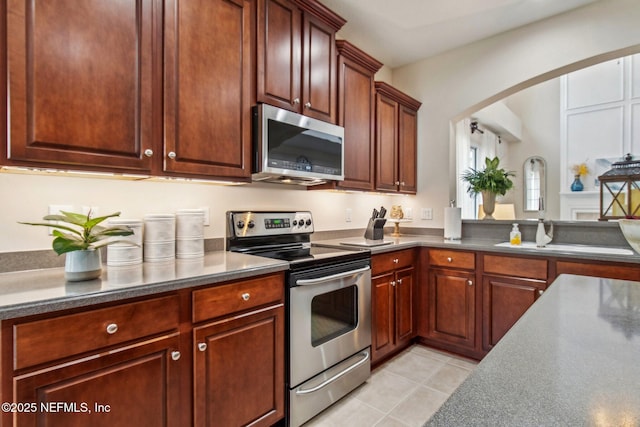 kitchen featuring stainless steel appliances, arched walkways, dark countertops, and light tile patterned floors