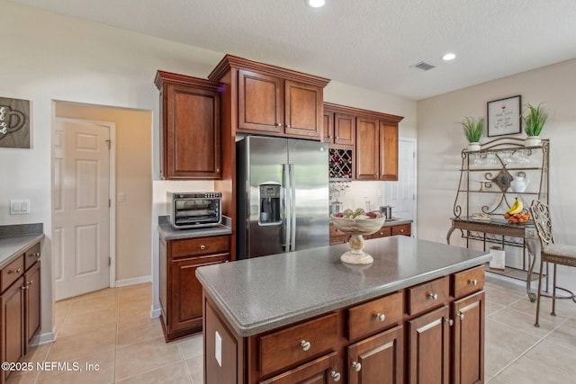 kitchen with light tile patterned flooring, a toaster, visible vents, stainless steel fridge with ice dispenser, and a center island