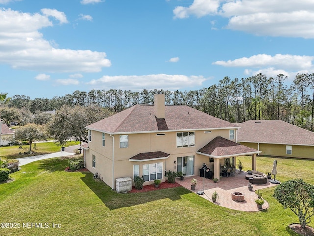 back of house with an outdoor fire pit, a chimney, a lawn, and a patio