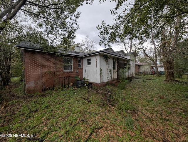 back of property featuring a yard, brick siding, and a chimney