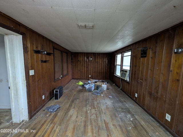 empty room with cooling unit, wood finished floors, visible vents, and wooden walls