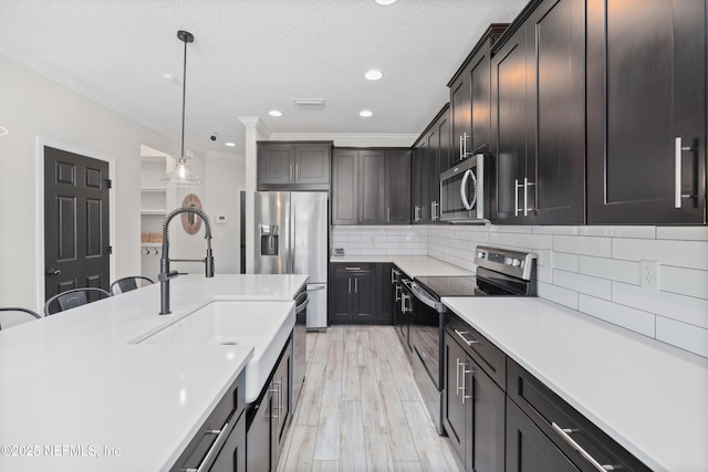 kitchen featuring decorative light fixtures, light countertops, decorative backsplash, appliances with stainless steel finishes, and a sink