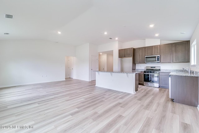 kitchen featuring light stone counters, stainless steel appliances, a kitchen island, visible vents, and vaulted ceiling