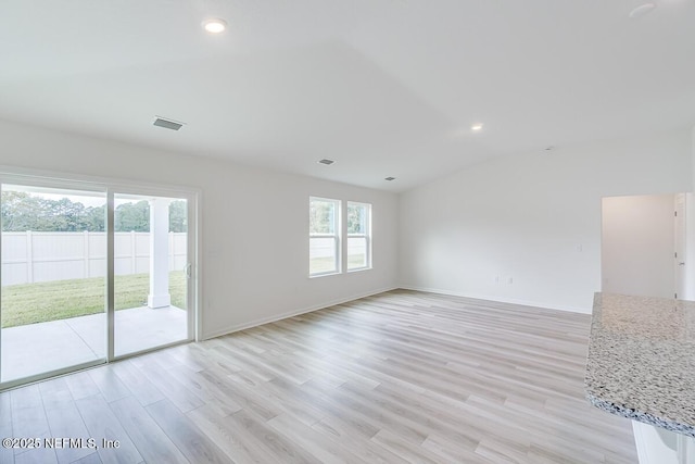 empty room with lofted ceiling, light wood-style flooring, and visible vents