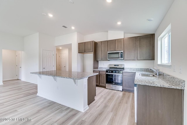 kitchen with stainless steel appliances, a kitchen island, light wood-type flooring, and a sink