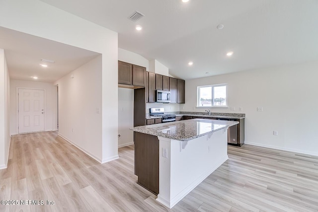 kitchen with a center island, visible vents, light wood-style flooring, appliances with stainless steel finishes, and light stone countertops