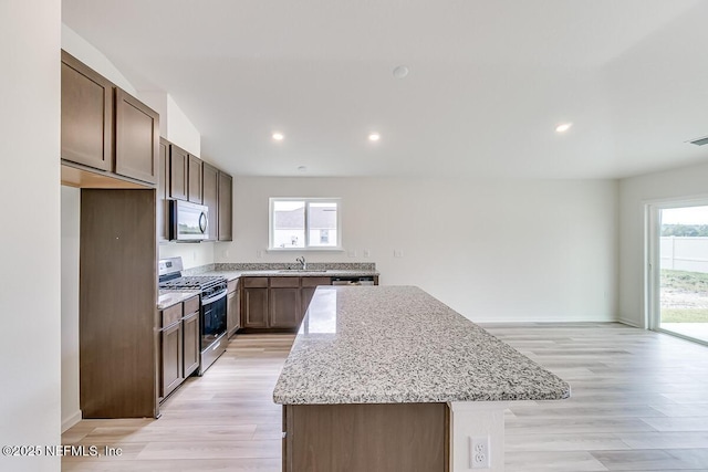 kitchen featuring a center island, light wood-style flooring, appliances with stainless steel finishes, a sink, and light stone countertops