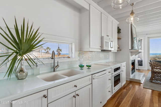 kitchen featuring light countertops, backsplash, a sink, wood finished floors, and white appliances